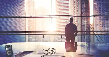 Business professional standing in an office looking out the window as the sun sets on the city.